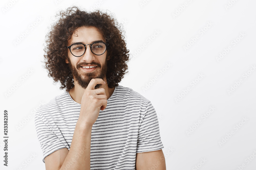 Chek it out. Intrigued attractive flirty guy in playful romantic mood, holding hand on beard, looking right and smiling with pleased curious expression, seeing something interesting and awesome Chek it out. Intrigued attractive flirty guy in playful romantic mood, holding hand on beard, looking right and smiling with pleased curious expression, seeing something interesting and awesome