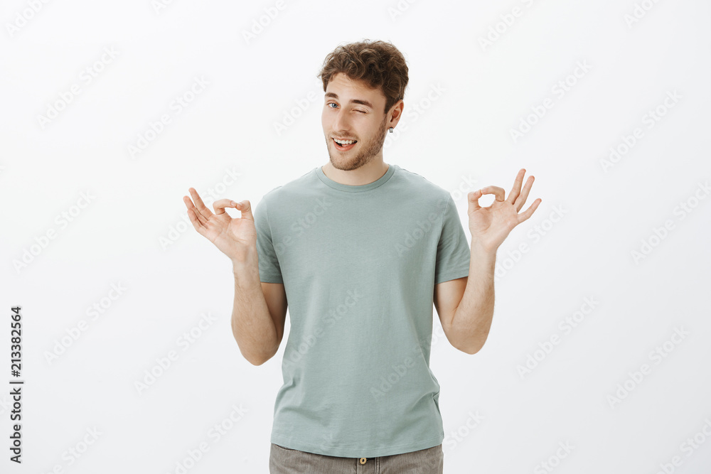 Charming confident boyfriend has everything under control. Portrait of chill good-looking adult guy in earrings, winking and smiling flirty while showing ok or okay gesture and calming down friend Charming confident boyfriend has everything under control. Portrait of chill good-looking adult guy in earrings, winking and smiling flirty while showing ok or okay gesture and calming down friend