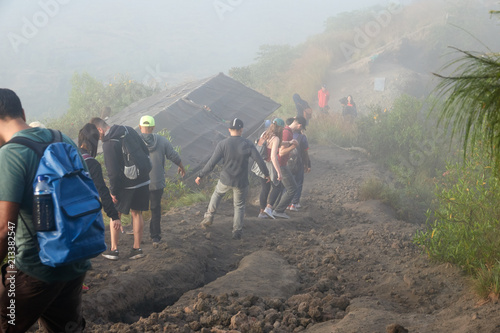 A group of tourists with backpacks coming down from the mountain on a summer morning in a strong fog. Indonesia, Bali, the volcano of Batur