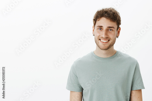 Portrait of satisfied happy Caucasian man in earrings and t-shirt, smiling broadly and gazing pleased at camera, talking casually with good friend, enjoying spending time with close people