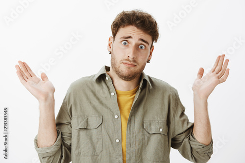 It was not my fault. Portrait of scared cute male model with beard and curly hair, raising palms in surrender, frowning and gazing with gloomy expression at camera, being uninvolved and unaware