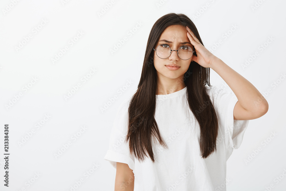Portrait of bothered tired Caucasian woman in trendy eyewear and white t-shirt, holding hand on temple and staring displeased at camera, feeling headache after overworking till late night Portrait of bothered tired Caucasian woman in trendy eyewear and white t-shirt, holding hand on temple and staring displeased at camera, feeling headache after overworking till late night