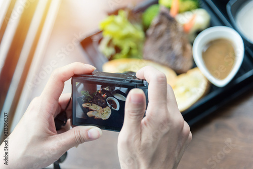 Woman taking food photo on camera at restaurant with rustic wood table. 