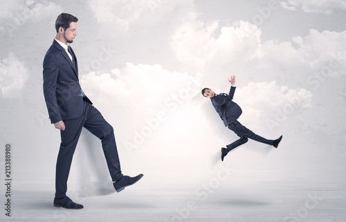 Big businessmen kicking himself as a small employee with cloudy background
