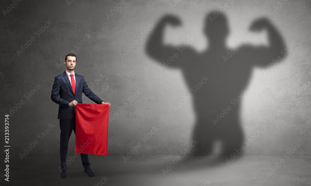 Fototapeta premium Businessman standing with red cloth on his hand and strong hero shadow on the background 