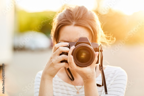 young girl taking pictures on camera in a summer Park at sunset photo