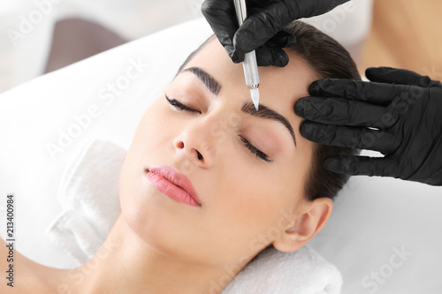 Young woman undergoing procedure of eyebrow permanent makeup in beauty salon