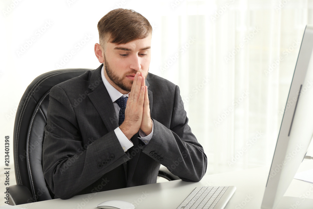 Naklejka premium Religious young businessman praying at table in office