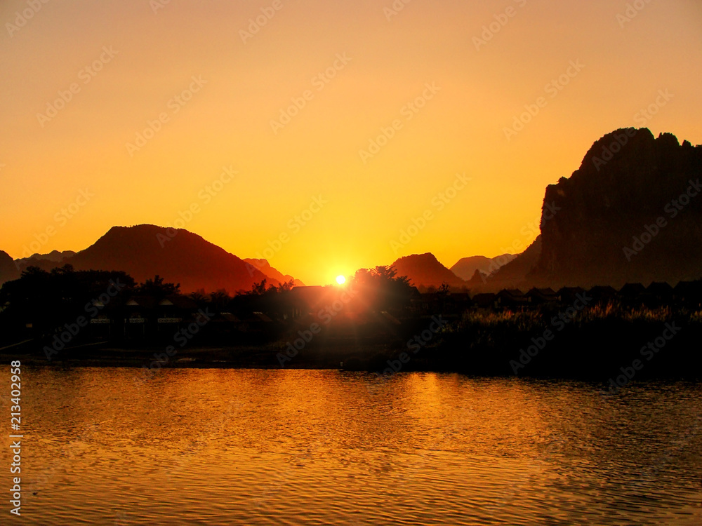Sunset over Nam Song River with silhouetted rock formations in Vang Vieng, Laos