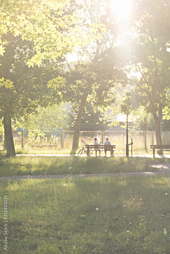 Mom and son are sitting on a bench in a park with a bicycle on a sunny day Mom and son are sitting on a bench in a park with a bicycle on a sunny day