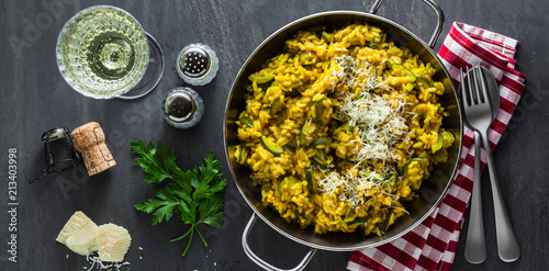 Fotografia banner of Italian dish yellow Risotto milanese with saffron, zucchini and Parmesan cheese on a black slate table with white wine in a glass