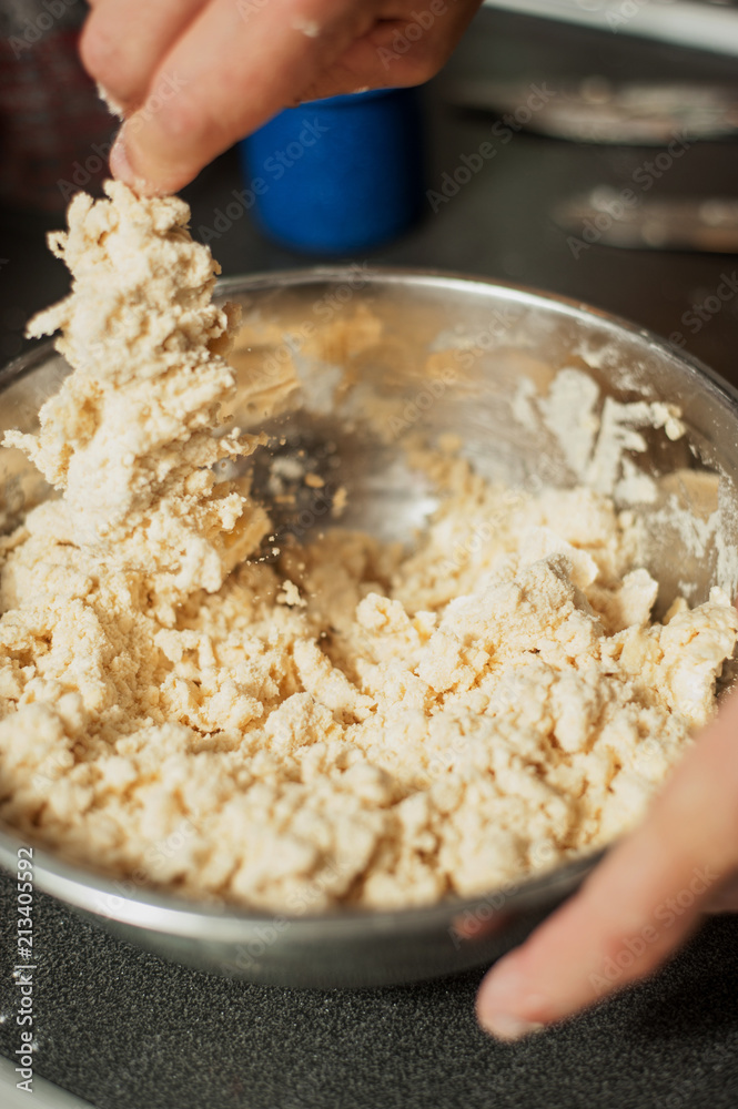 A man stirs ingredients in a metal bowl to make pastry dough. The process of making apple pie. Vertical image with shallow depth of field. A man stirs ingredients in a metal bowl to make pastry dough. The process of making apple pie. Vertical image with shallow depth of field.
