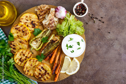 Grilled vegetables, fresh herbs, sauce on a wooden tray. Healthy food. A delicious appetizer. Top view.