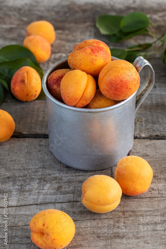 Delicious ripe apricots in aluminum mug on wooden table, rustic.