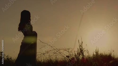 Silhouette of elvish queen walking on the meadow and thinking during beautiful sunset. Lovely woman peacefuly walking alone in forest.
