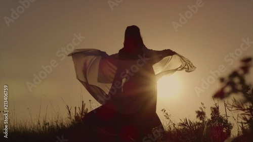 Silhouette of a queen posing in a dress with a beautiful headscarf. Femal elf is spinning in slow motion during sunset. Soft light. Tale.