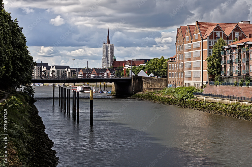 Obraz premium Bremen, Germany - Red brick waterfront buildings and huge bridge across the river Weser with church spire in the distance