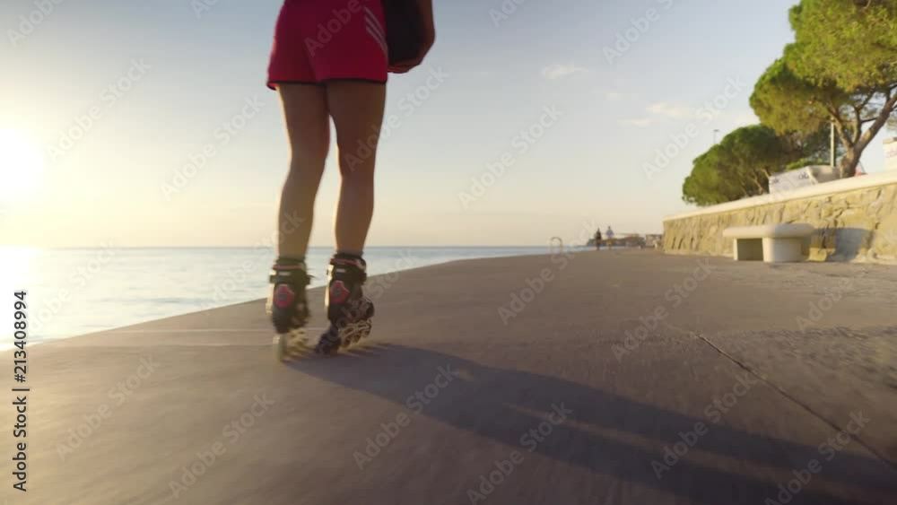 Young caucasian woman roller skating in the sunset at the sea, shot following legs, low angle