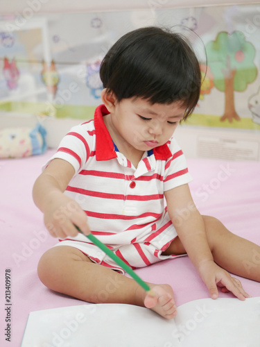 Little Asian baby girl, 15 months old, learning to hold a pencil and drawing on a book - pencil grasp development begins when children are babies
