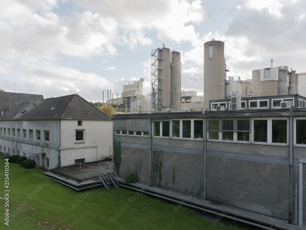 A large gray factory with green trees and lawn in the autumn in clear weather