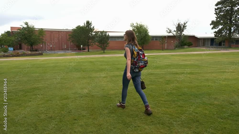 A female college student walking across a lawn on campus A female college student walking across a lawn on campus