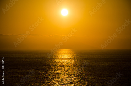 Yellow hazy sunset over a dark, reflective sea