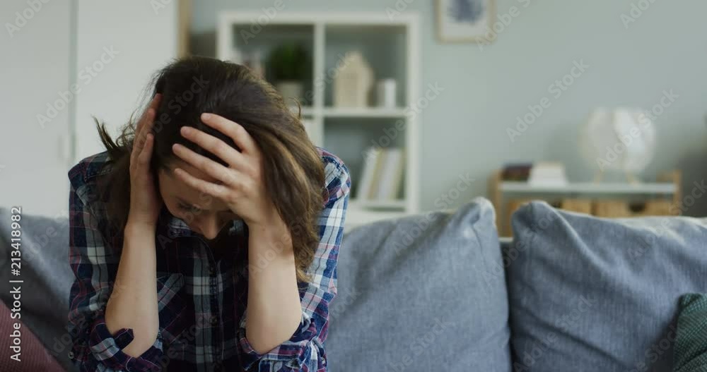Young woman crying while sitting on the couch at home, then lying on it and pills with water being on the first plan in front of the camera. Young woman crying while sitting on the couch at home, then lying on it and pills with water being on the first plan in front of the camera.