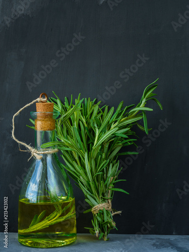 A bottle of rosemary oil with fresh rosemary bunch on a dark stone background