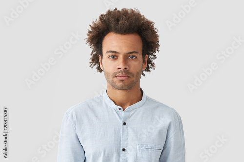 Serious self assured mixed race male with curly hair, looks with concentrated expression, dressed in white shirt, listens attentively recommendations from colleague to improve financial situation © wayhome.studio 