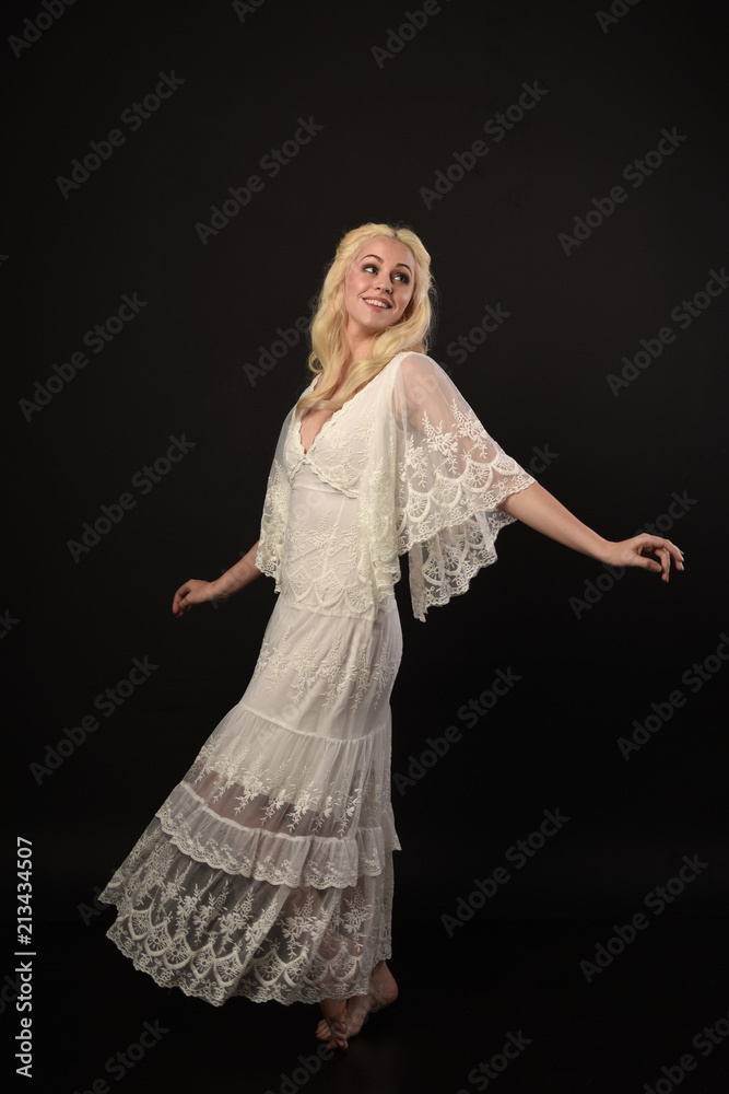 full length portrait of blonde girl wearing white lace dress. standing pose. black studio background. full length portrait of blonde girl wearing white lace dress. standing pose. black studio background.