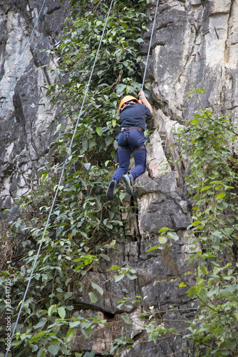 Asian boy in the helmet climbs the rock, kid rock climber sports outdoors.