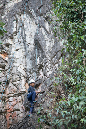 Asian boy in the helmet climbs the rock, kid rock climber sports outdoors.