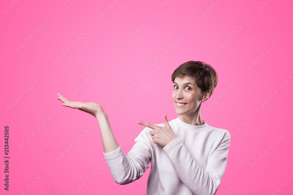 Excited girl pointing showing at pink background with copy space. Young beautiful happy smiling and laughing woman Excited girl pointing showing at pink background with copy space. Young beautiful happy smiling and laughing woman