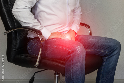 A man sits in an office chair and holds on to the groin, crotch, prostatitis photo