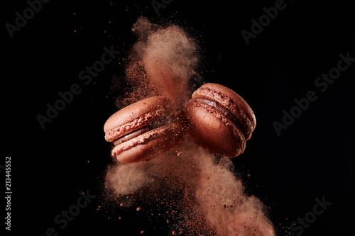Macaron explosion. French chocolate macaron with cocoa powder against black background
