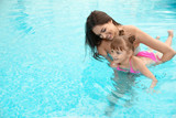 Happy mother teaching her daughter to swim in pool