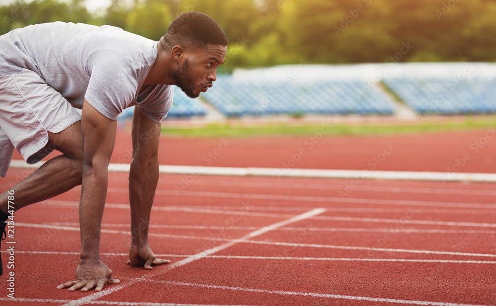 African-american male sportsman ready to run on stadium track