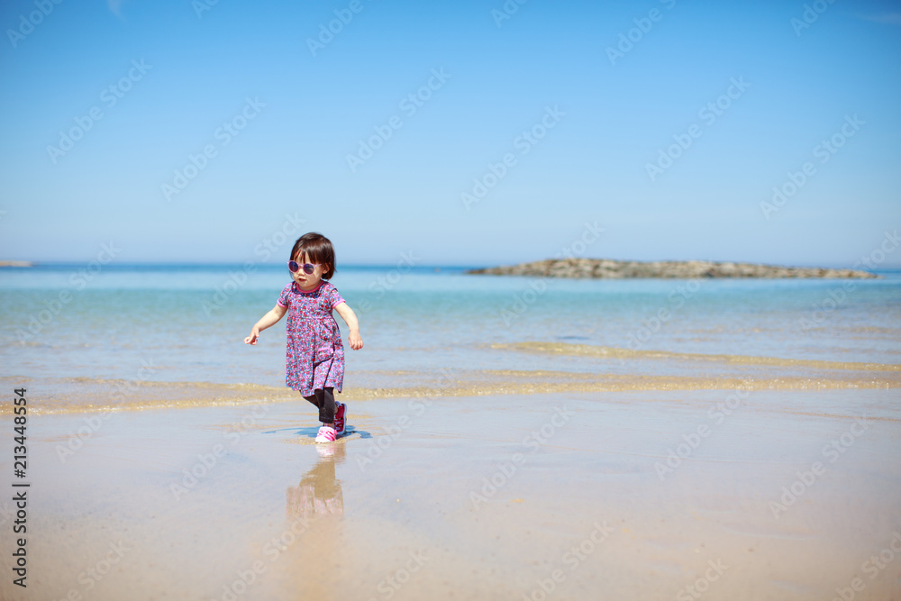 baby girl wearing sunglasses running on the summer beach