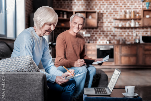 Bill calculation. Cheerful blonde keeping smile on her face while working at home
