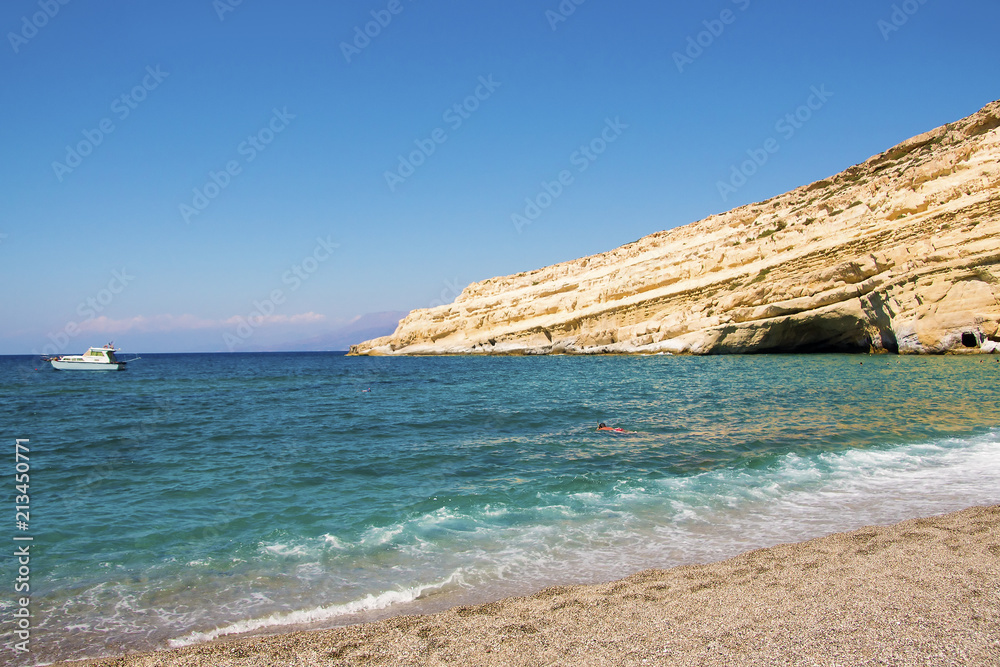 Fototapeta premium Deserted Matala beach with lonely swimmer in a sunny summer day. Crete, Greece