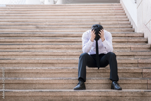Asian businessman professional failed or upset in his job and sitting on staircase. Business problem concept.