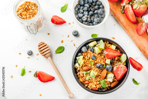 Healthy breakfast with muesli or granola with nuts and fresh berries and fruits - strawberry, blueberry, kiwi, on white table, copy space top view