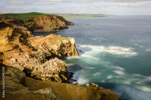Elevated view of red sandstone cliffs illuminated by late afternoon light on the Chatham Islands, New Zealand. Long exposure.