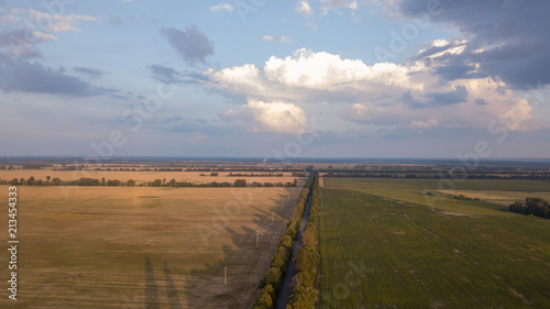 Aerial panorama of rural road passing through agricultural land and canola fields in Australian countryside at sunset