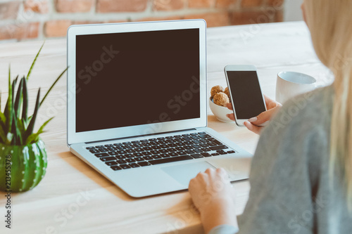 Back view of woman using smart phone and laptop at home