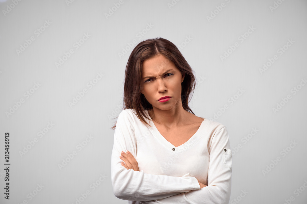 Waist-up portrait of beautiful girl with dark straight hair frowning her face in displeasure, wearing loose long-sleeved sweater, keeping arms folded. Attractive young woman in closed posture. Waist-up portrait of beautiful girl with dark straight hair frowning her face in displeasure, wearing loose long-sleeved sweater, keeping arms folded. Attractive young woman in closed posture.