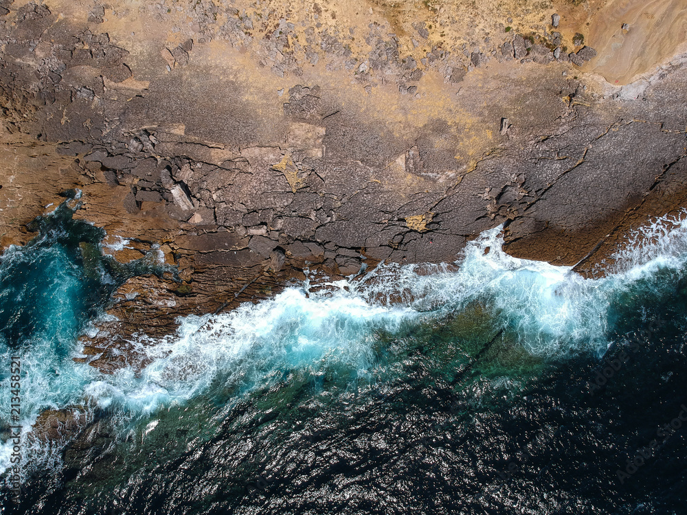 Aerial top view of sea waves hitting rocks on the beach with turquoise sea water. Amazing rock cliff seascape in the Portuguese coastline. Drone shot.
