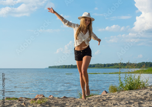 Beautiful happy young woman in a hat and in shorts running along the seashore