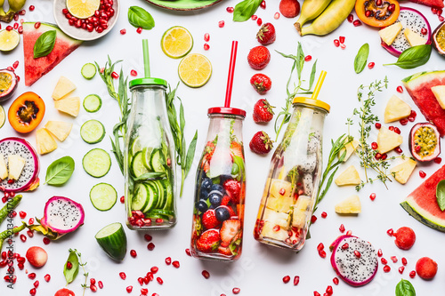 Summer clean and healthy lifestyle and fitness background with various infused water in bottles, colorful sliced ingredients: fruits, berries, vegetables, herbs on white background, top view
