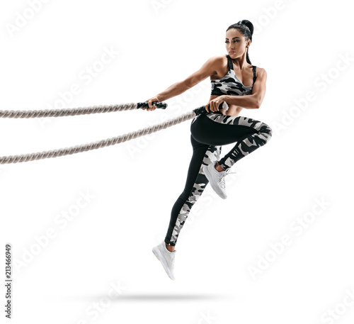Muscular woman jumping with heavy ropes. Photo of latin woman in military sportswear isolated on white background. Strength and motivation.